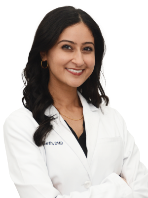 A woman in a white lab coat stands confidently with her arms crossed.